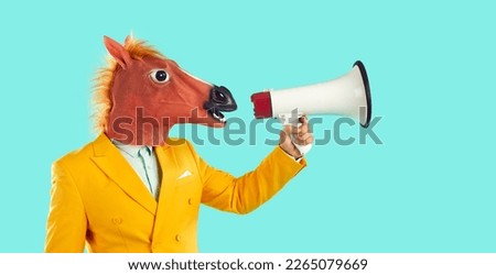Side view young man in trendy yellow suit and funny crazy masquerade horse face mask standing on blue studio background, speaking through megaphone with loud voice, sharing message, inviting to event