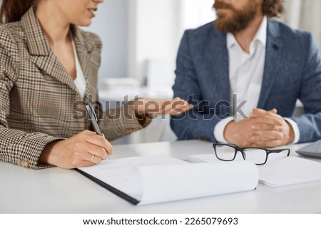 Two people meet and discuss business contract. Woman sitting at office desk with some paper documents, holding pen in her hand, talking to her client, or making good offer to her business partner