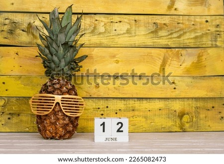 Creative june calendar planner with number  12. Pineapple character on bright yellow summer wooden background with calendar cubes.