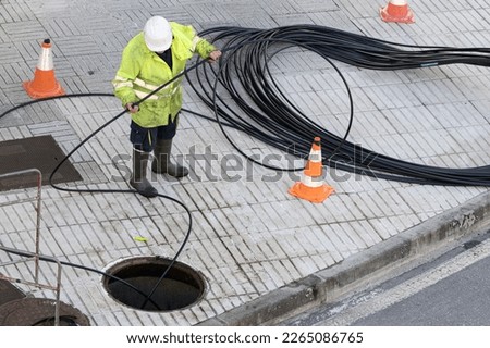 A worker is performing maintenance tasks on a communication cable located on the sidewalk of a city Royalty-Free Stock Photo #2265086765