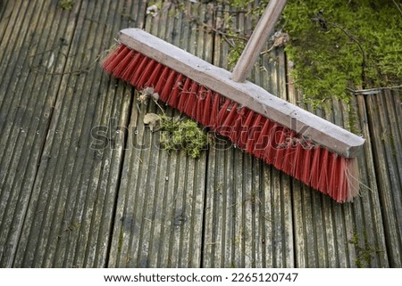 Red outdoor broom with stiff plastic bristles on a dirty wooden deck with algae and moss, spring cleaning in garden and yard for the new season, copy space, selected focus, narrow depth of field Royalty-Free Stock Photo #2265120747