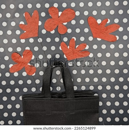 Five red paper flowers on black fabric bag. Black and white dotted background