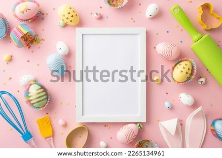 Easter concept. Top view photo of empty photo frame rolling pin whisk brush colorful easter eggs in paper baking molds easter bunny ears and sprinkles on isolated pastel pink background with copyspace