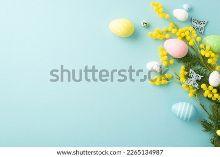 Easter concept. Top view photo of colorful easter eggs yellow mimosa flowers and butterflies on isolated pastel blue background with copyspace