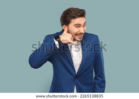 Portrait of happy positive man with mustache standing showing call me back gesture, flirting with beautiful woman, wearing official style suit. Indoor studio shot isolated on light blue background.