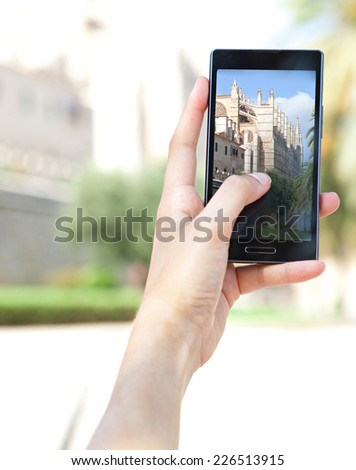 Close up of a young woman hand holding a smart digital phone device taking pictures of a characterful architecture cathedral, visiting a destination city on holiday. Vacation technology lifestyle.