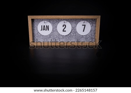 A wooden calendar block showing the date January 27th on a dark black background, save the date or date of event concept