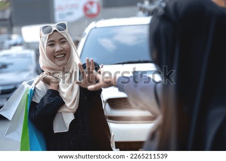 Muslim woman raise her hands to greet her friend at Sunday market, Lifestyle of Muslim women in hijab shopping together on weekends