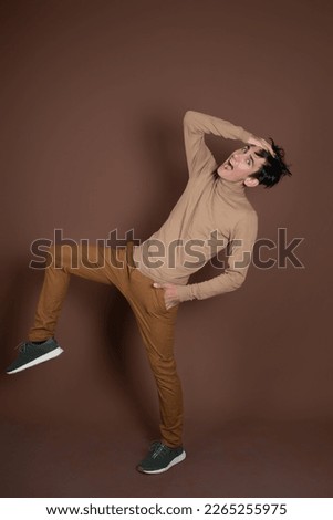 Young attractive guy fooling around in the studio. Brown background.
