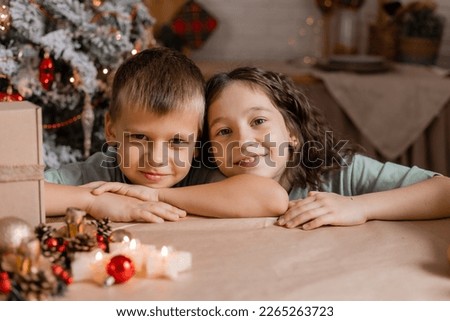 children, a boy and a girl write a letter with Christmas wishes to Santa Claus, sitting at a wooden kitchen table. High quality photo