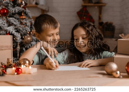 children, a boy and a girl write a letter with Christmas wishes to Santa Claus, sitting at a wooden kitchen table. High quality photo