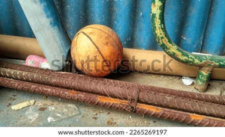 A tiny basketball sitting on a pile of metal in the yard of a junkyard.