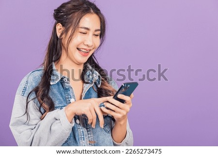 Portrait of Asian beautiful young woman confident wear denim jeans shirt hold smartphone typing smartphone, Happy lifestyle female write message look phone, studio shot isolated on purple background
