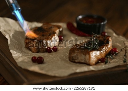 Cooking meat medallions with manual gas burner on wooden table in photo studio, closeup. Food stylist