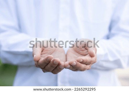 
Close-up shot of a man wearing a white long-sleeved shirt. who opens both hands to support something or request something Selective focus within the palm