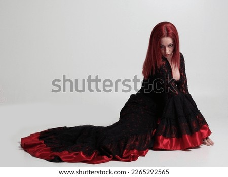 portrait of beautiful red haired woman wearing long black fantasy vampire costume gown, isolated pose on  studio background.