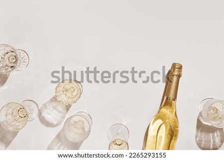 Flat lay with white sparkling wine bottle, set glasses wine with sunshine shadow and flare on light beige background. White wine aesthetic photo, copyspace. Summer holiday monochrome color still life Royalty-Free Stock Photo #2265293155