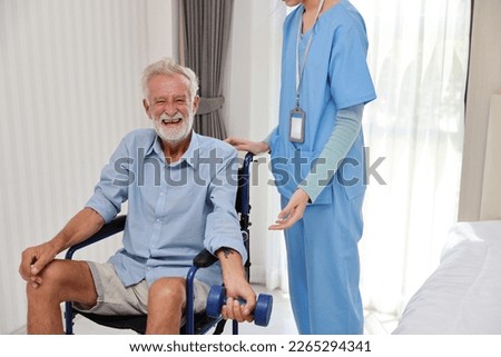 Happy caregiver helping senior elderly man lifting dumbbell and excercise with wheelchair at home or retirement house. Asian smiling nurse taking good help care and support of elder patient at house.