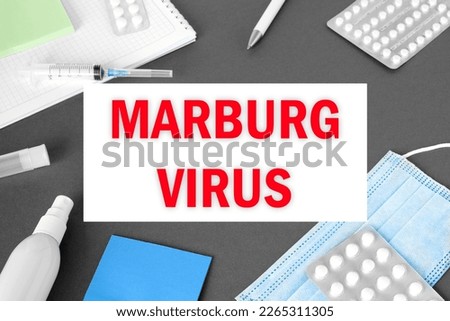 The word Marburgvirus on Gray modern doctor desk table background. Mask, notepad, syringe, sanitizer and supplies. MARV, Marburg Virus spreading. Medicine and healthcare, medical education. Top view