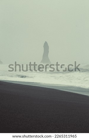 Old rock on Reynisfjara beach monochrome landscape photo. Beautiful nature scenery photography with fog on background. Idyllic scene. High quality picture for wallpaper, travel blog, magazine, article