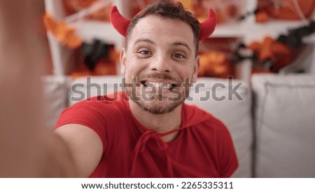 Young caucasian man wearing devil costume taking selfie picture at home