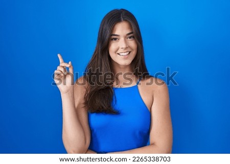 Hispanic woman standing over blue background with a big smile on face, pointing with hand finger to the side looking at the camera. 