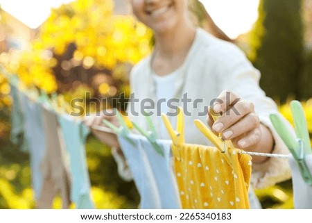 Closeup view of smiling woman hanging baby clothes with clothespins on washing line for drying in backyard Royalty-Free Stock Photo #2265340183
