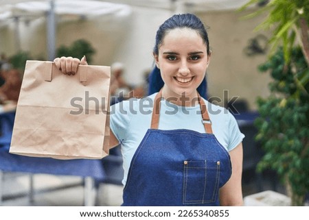 Young caucasian woman waitress smiling confident holding take away food at coffee shop terrace