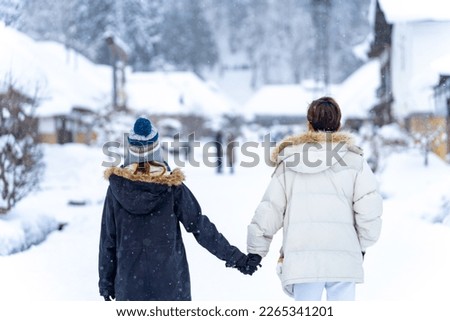 Asian couple holding hands walking together during travel Ouchi-juku village in Fukushima prefecture covered in snow. Man and woman enjoy outdoor lifestyle travel Japan on winter holiday vacation.