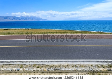 Asphalt road and lake with mountain natural scenery in Xinjiang, China.