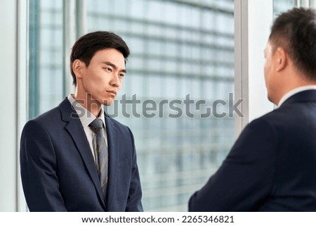 two asian businessmen standing by the window in modern office having a discussion conversation, side view Royalty-Free Stock Photo #2265346821