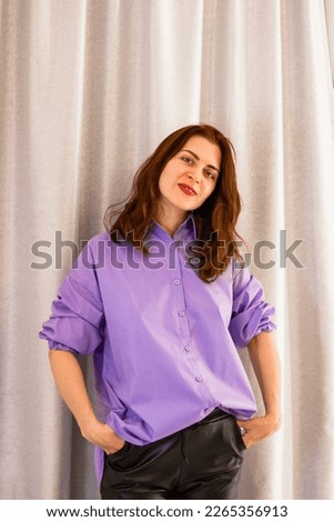 Candid lifestyle portrait of young woman with red hair in casual clothing on gray background, with copy space.