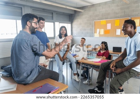 Group of teenager students with young teacher at classroom, sitting talking and sharing conversation together