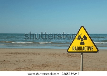 Radioactive pollution. Yellow warning sign with hazard symbol near contaminated area on beach. Space for text