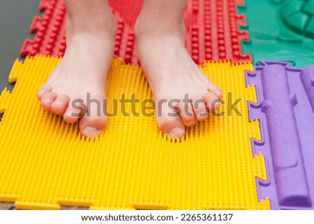child does leg exercises on orthopedic massage mat at home. Puzzle mats imitating different textures for baby foot massage. Prevention of flat feet and hallux valgus in child. Medicine. Health care.