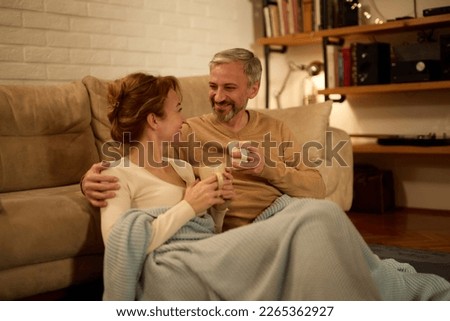 Mature couple drinking tea while sitting in the living room at night