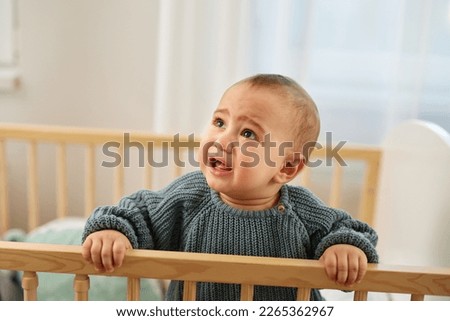 Adorable toddler standing in the crib crying