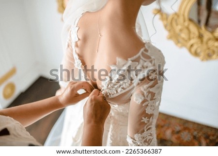 Gorgeous, blonde bride in white luxury dress is getting ready for wedding. Morning preparations. Woman putting on dress. Royalty-Free Stock Photo #2265366387