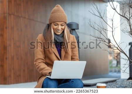 Side view of young woman chatting online on laptop computer, sitting on bench, young female freelancer chatting on social media