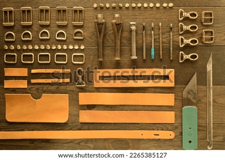 Leather workshop, handbag manufacturing industry, hand craft. Numerous metal elements bag hardware indoors. Leather pieces on wooden table. Work tools for leather handicraft. Table top view. Royalty-Free Stock Photo #2265385127