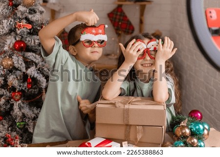 children, a boy and a girl in carnival glasses are live streaming for social networks with the unpacking of Christmas gifts. High quality photo