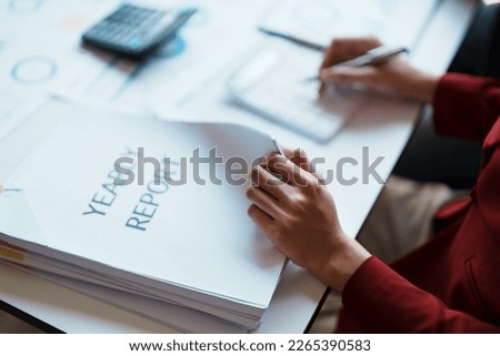 Businesswoman reviewing annual documents and using calculator to calculate budget and profit