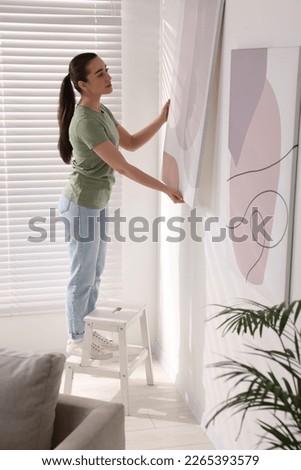 Woman on ladder hanging picture at home