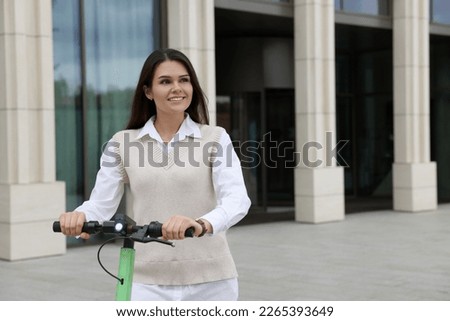 Businesswoman riding electric kick scooter on city street, space for text