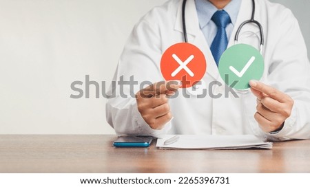 Yes or No. A doctor holding red and green papers with a checkmark and a cross while sitting at the table in the hospital. True and false symbols accept and rejected for evaluation. Close-up photo