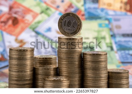 Columns of many coins in denominations of 100 Kazakhstani tenge against the background of Kazakhstani banknotes