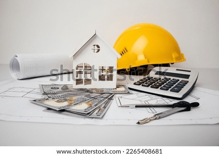 Yellow helmet, money and model of house on drawings. Building and costs concept.