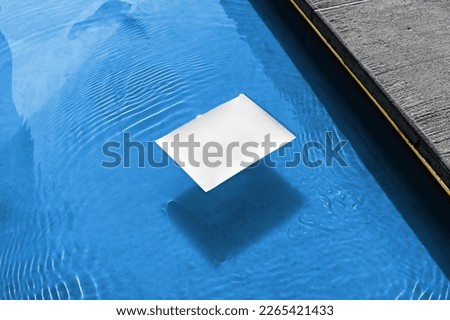 Poster mockup template floating in the blue water pool. Isolated surface to place your design.  Royalty-Free Stock Photo #2265421433