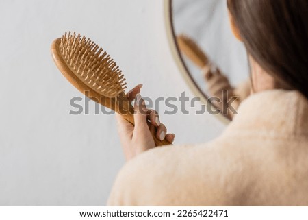 cropped view of young woman holding hairbrush near blurred mirror in bathroom Royalty-Free Stock Photo #2265422471