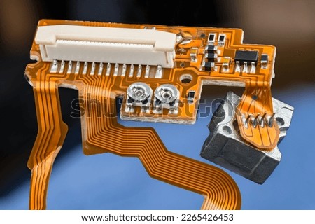 Orange printed circuit board with flex ribbon cables, small electronic components and white connector. Closeup of flat and bendy PCB from inside of digital CD-DVD optical disc drive. E-waste disposal. Royalty-Free Stock Photo #2265426453